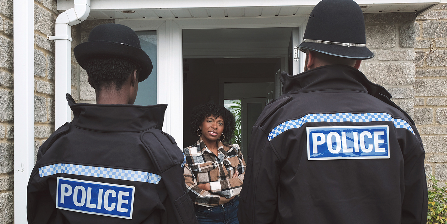 Two police officers in unform talk to a person standing in a doorway.